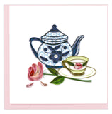 A teapot with blue floral swirls, a full teacup, and a pink rose laying beside them.
